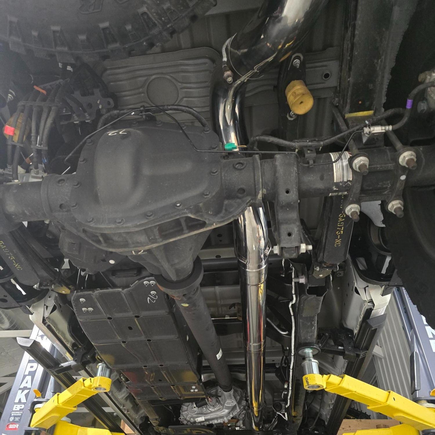 Undercarriage of a vehicle with yellow suspension components in a workshop setting